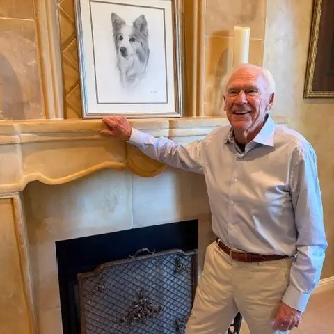 Photo of Rich Avanzino in his home with a framed portrait of his dog, Sido